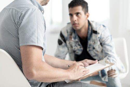 Close-up of counselor taking notes while analysing behavior of young man