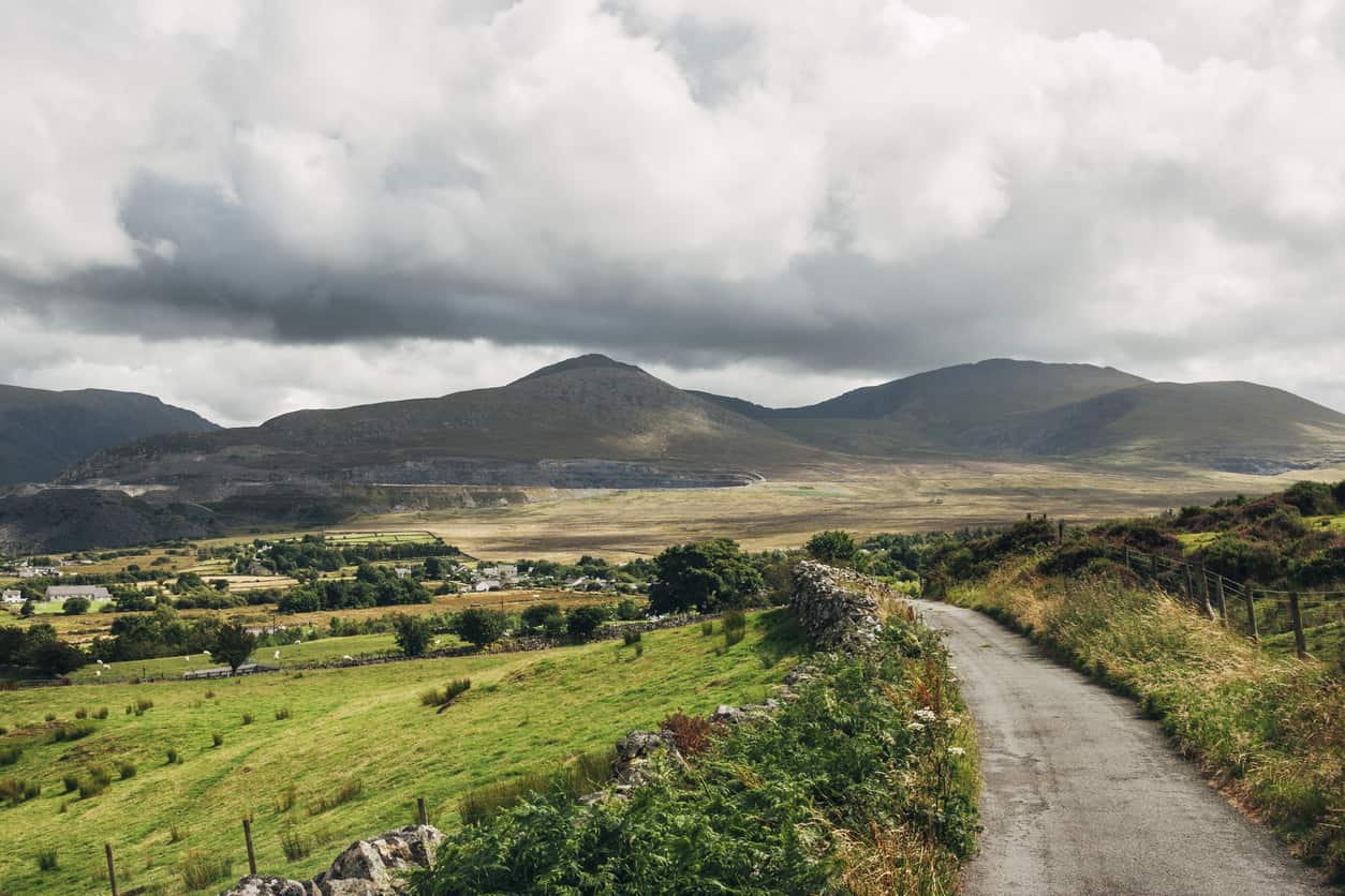 A rural road, surrounded by fields, leading toward mountains in the distance
