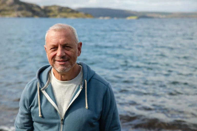 recovery Scotland. A waist-up shot of a mature male smiling at the camera in the rural coastal setting of Scotland.